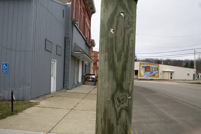 A weathered wooden telephone pole splitting a small-town street scene under a grey cloudy sky