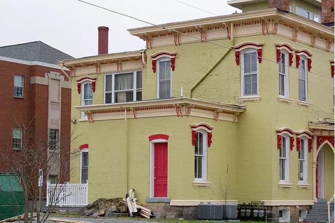 A yellow-green building with ornate red trim photographed at an angle beside a brick building