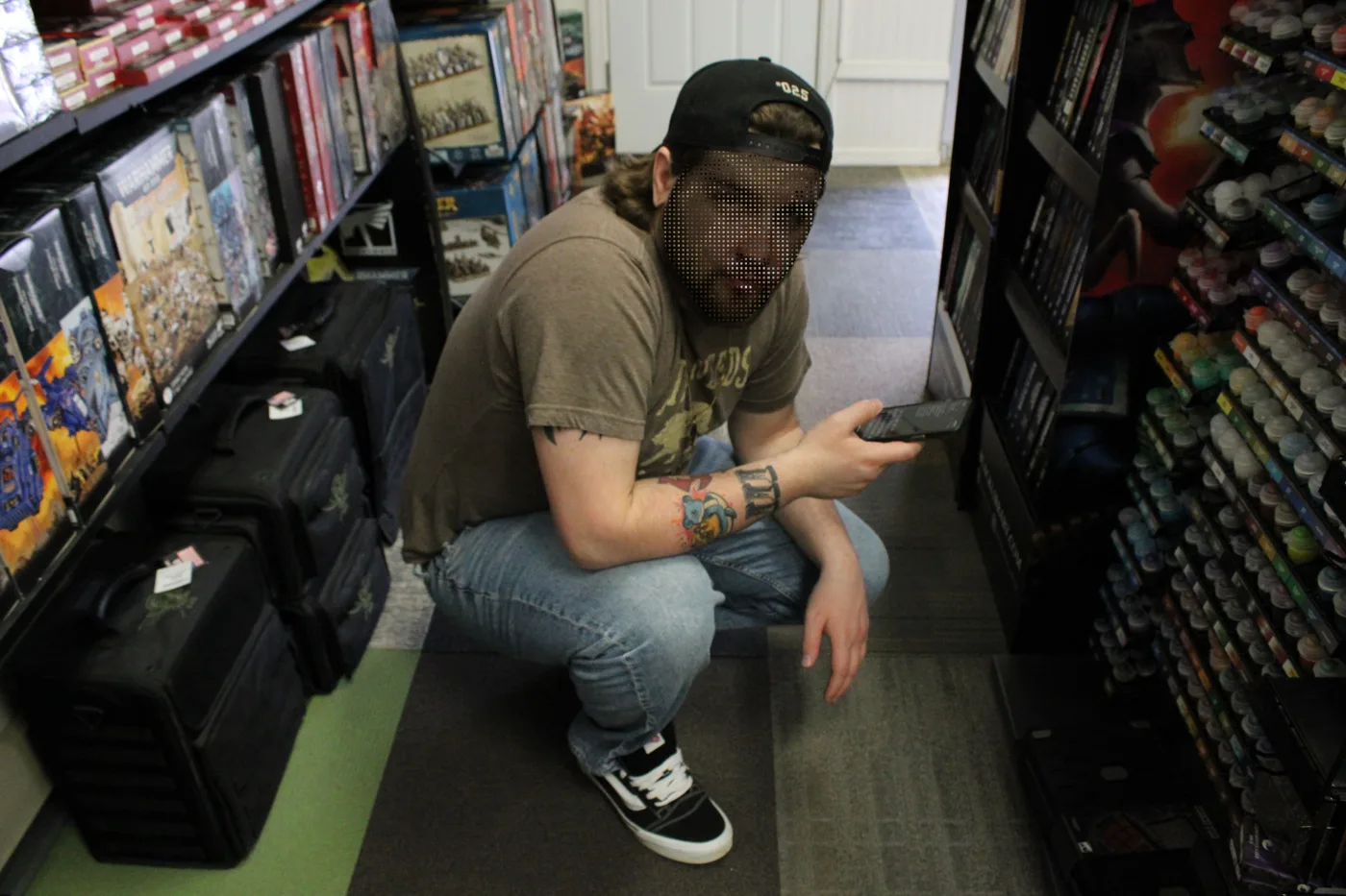 A person squatting in a game store aisle holding a model, their face replaced with a pixelated pig face
