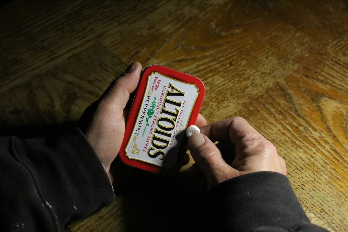 Hands holding a red tin of peppermint mints over the same wooden table