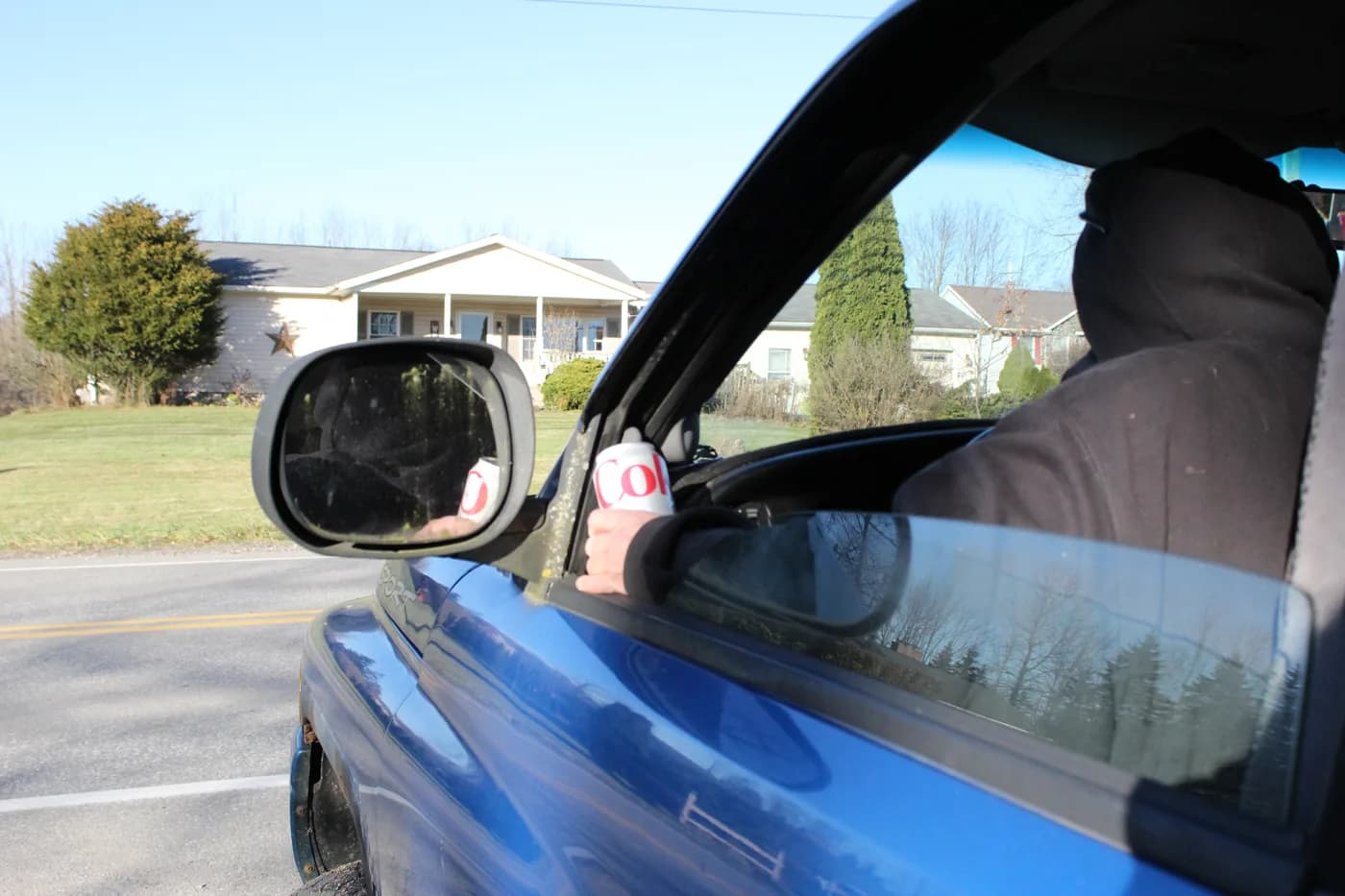 The hooded figure in the truck holding a can of soda instead, facing forward toward the road