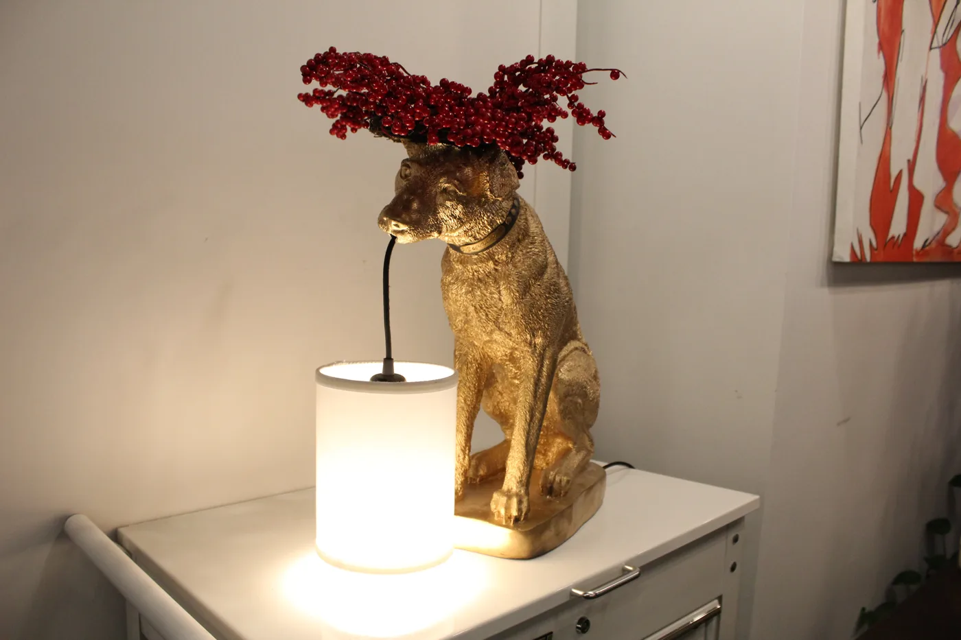 A gold dog statue lamp with red berries behind its head, lighting up a dark corner of the shop