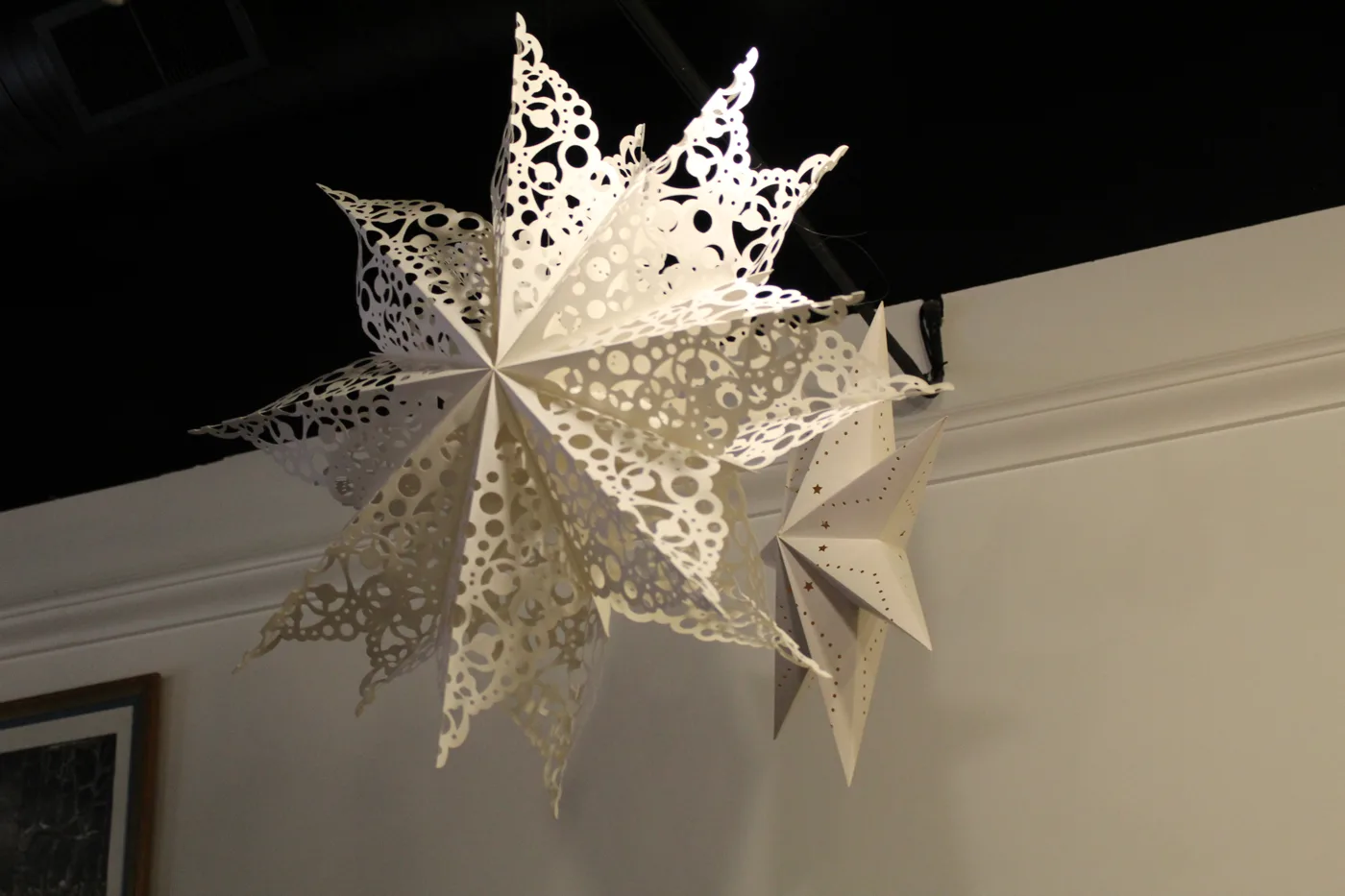 White paper snowflake stars hanging from a dark ceiling, casting shadows onto the wall below