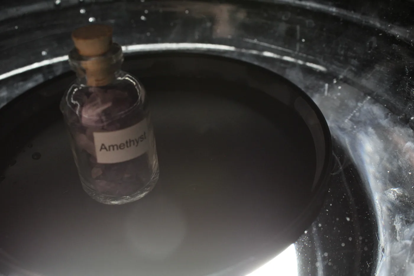 The amethyst bottle standing in a glass bowl of water, seen from above with a soft bokeh of light on the surface