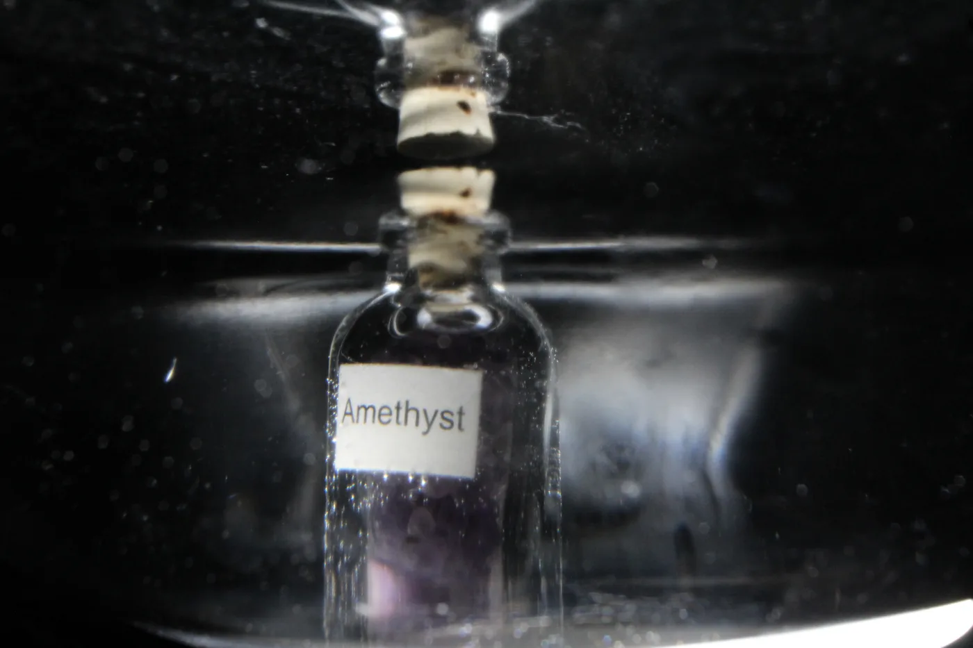 The amethyst bottle viewed through the side of the glass bowl, distorted by the water