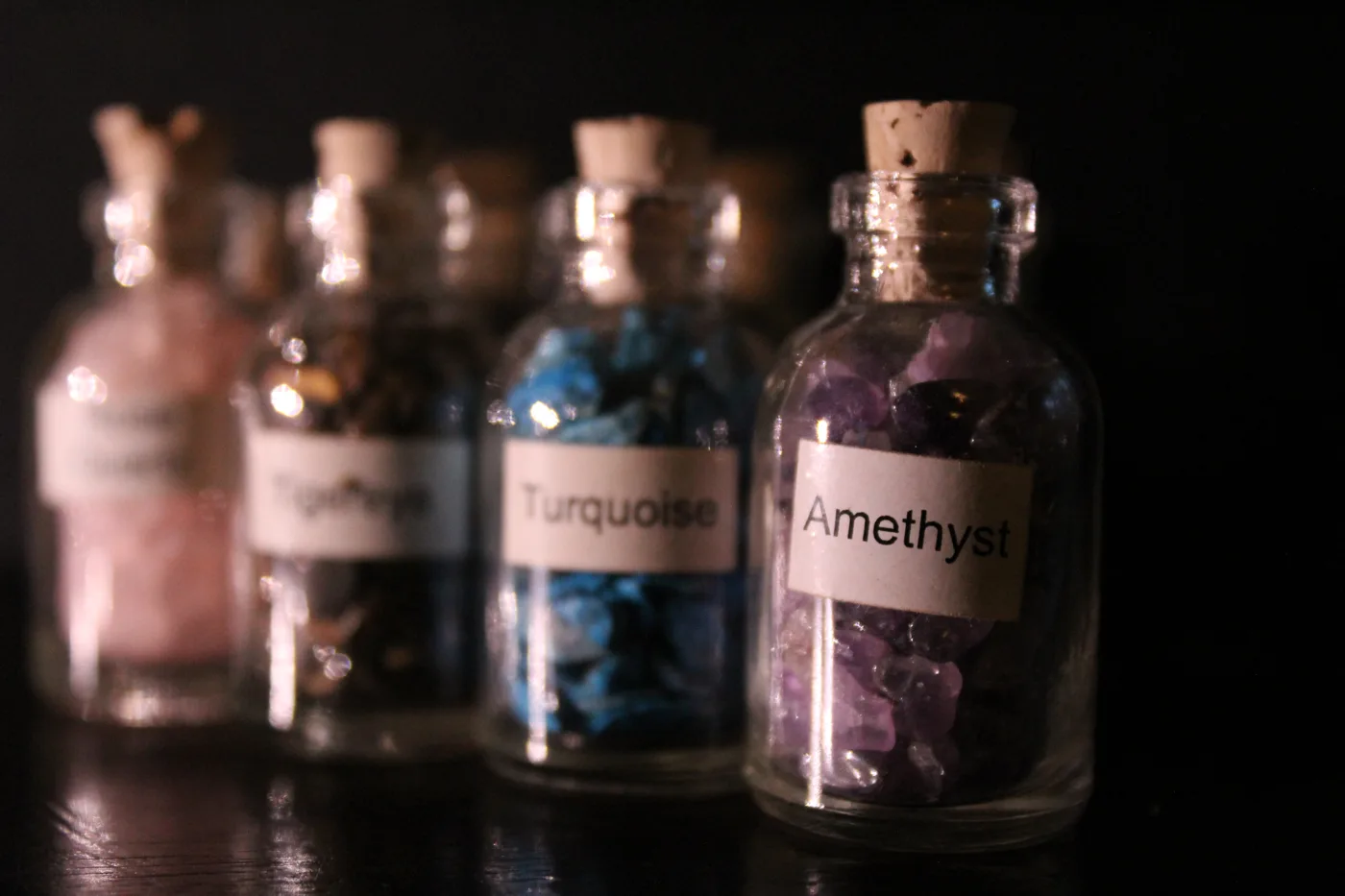 Labeled bottles of turquoise and amethyst stones catching light against a dark background, the others fading out of focus