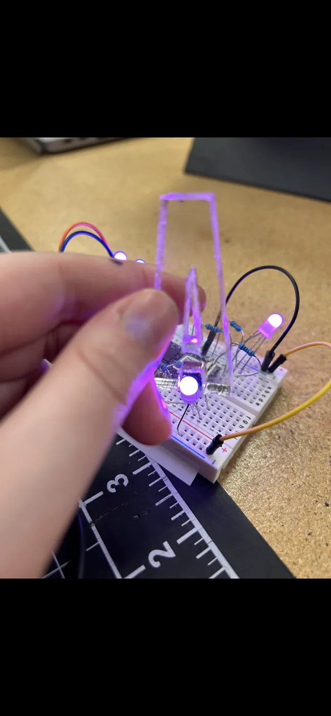 A clear acrylic letter held over a breadboard, glowing purple from an RGB LED