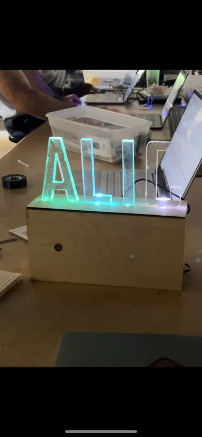 The finished ALIC sign glowing teal and blue on its wooden base